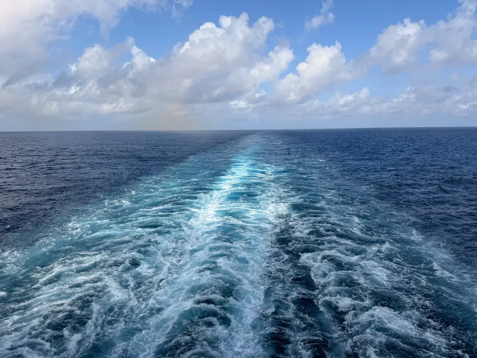 A cruise ship wake stretching across deep blue ocean toward the horizon